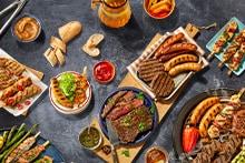 Gevulde barbecue tafel met verschillende soorten gegrild vlees, worstjes, spiesjes, groenten, dips, brood en een glas drinken.