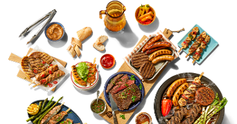 Gevulde barbecue tafel met verschillende soorten gegrild vlees, worstjes, spiesjes, groenten, dips, brood en een glas drinken.
