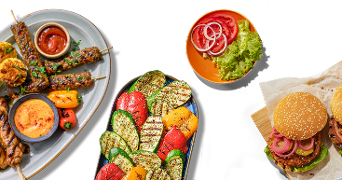 Platte met gegrilde groenten, spiesjes met sausjes, hamburgerbroodjes met sla, tomaat en ui, en een schaaltje met sla, tomaat en ui.