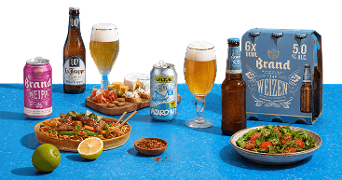Assortiment van speciaalbieren, waaronder Brand NEIPA, La Trappe Trappist, Uiltje Wizard Wit en Brand Weizen, geserveerd naast borrelhapjes, noedels met groenten en vlees, en een salade, op een blauwe ondergrond.