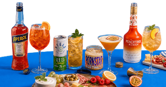Een selectie van zomerse cocktails en ingrediënten, met A-merken als Aperol, Peachtree en Stël Iced Tea Lemon, diverse frisse drankjes in glazen met garnering, een Pornstar Martini mix, verse vruchten en een borrelplank met kaas, vleeswaren en olijven op een blauwe ondergrond.