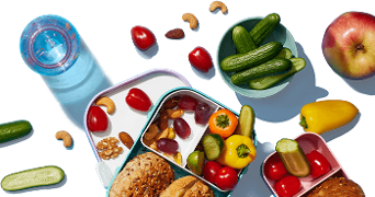 Broodtrommel gevuld met groenten, fruit en noten naast een fles water en vers fruit.