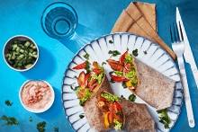 Twee wraps gevuld met kip en groenten op een bord, geserveerd met bijgerechten en een glas water.