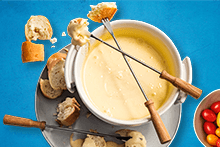 Kaassfondue in een witte fonduepan met stukjes brood op een bord, samen met bakjes kleurrijke snoeptomaatjes en worteltjes