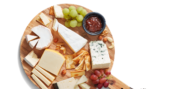 Kaasplank met verschillende soorten kaas, crackers, druiven, noten en een bakje jam op een houten serveerplank.