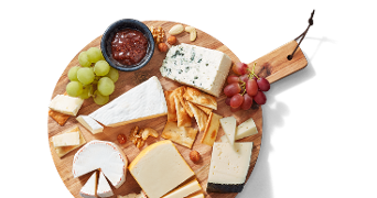 Kaasplank met verschillende soorten kaas, crackers, druiven, noten en een bakje jam op een houten serveerplank.