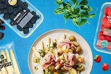Collage van Albert Heijn producten: bramen in plastic verpakking, spinaziebladeren, Nederlandse aardbeien in plastic verpakking, witte asperges in verpakking, en een bord met een gerecht van witte asperges, aardappelen, ham en groenten.