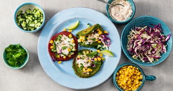 Borden en kommetjes met mais, komkommer, koolsla en pannennkoekjes met dit erop.