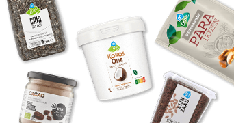 Verschillende verpakkingen met biologische noten, zaden, cacao en kokosolie van Albert Heijn verspreid op een zwarte achtergrond