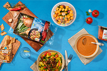 Selectie van Albert Heijn producten en maaltijden, zoals een groentepakket, soep, salade, tomaten, wortelreepjes en stokbrood, op een donkere ondergrond gepresenteerd