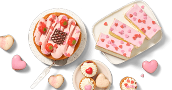 Assortiment van gebak en koekjes met roze en hartvormige decoraties, waaronder een taart met aardbeien, gebakjes met roze glazuur en hartjes, en slagroomsoesjes.