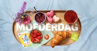 Ontbijt op een houten dienblad met bloemen, een croissant, aardbeien, roze macarons, thee en de tekst 'MOEDERDAG 11 mei'.