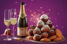 Feestelijke oud en nieuw setting met een schaal oliebollen, een fles Grande Pierre champagne, twee champagneglazen en vuurwerk op de achtergrond