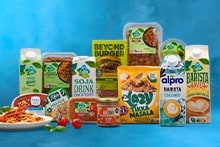 Assortiment van plantaardige producten zoals AH Terra soja yoghurt, rulggehakt, sojadrink, tempeh, avocado stukjes, en bekende merken zoals Beyond Burger, Alpro Barista en Lazy Tikka Masala. Vooraan een bord pasta met tomaat en basilicum.