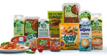 Assortiment van plantaardige producten zoals AH Terra soja yoghurt, rulggehakt, sojadrink, tempeh, avocado stukjes, en bekende merken zoals Beyond Burger, Alpro Barista en Lazy Tikka Masala. Vooraan een bord pasta met tomaat en basilicum.