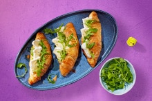 Verschillende paasbrunch gerechten, waaronder gevulde eieren in bladerdeeg, broodjes met roomkaas en rucola, en gepaneerde eieren met dooier, geserveerd op kleurrijke borden.