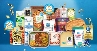 Winnaars van de Vries Vers verkiezing 2025 bij Albert Heijn: diverse bekroonde AH-huismerkproducten, zoals sojayoghurt, halfvolle melk, groentefriet, Gyoza, kant-en-klaarmaaltijden, kaas en meer, uitgestald met confetti en medailles tegen een blauwe achtergrond.