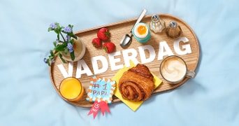 Vaderdag ontbijt met croissant, koffie, zachtgekookt ei, sinaasappelsap en aardbeien op dienblad met bloemen en de tekst "Vaderdag".
