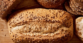 Volkorenbrood met zaden op een houten ondergrond, omringd door andere broodsoorten.