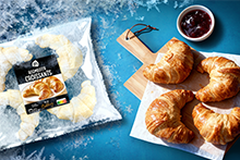 Zak met AH roomboter croissants, vier afgebakken croissants op een houten plank met een schaaltje jam erbij