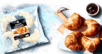 Zak met AH roomboter croissants, vier afgebakken croissants op een houten plank met een schaaltje jam erbij