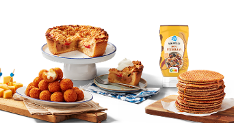 Verschillende typisch Nederlandse lekkernijen, waaronder een stuk appelkruimeltaart met slagroom, een schaal bitterballen, blokjes kaas met prikkers, een stapel stroopwafels, en een fles AH pindakaas op de achtergrond.