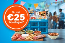 Blauwe Albert Heijn krat gevuld met diverse borrelproducten, zoals chips van Tyrrells, noten van John & Cashew, een fles water, en dips, met een houten plank met vleeswaren, kaas, crackers, olijven en een oranje label waarop staat “Nu met €25 borreltegoed”.