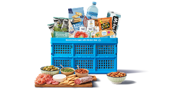 Blauwe Albert Heijn boodschappenkrat gevuld met diverse A-merken en huismerk producten, omgeven door een borrelplank met kaas, vleeswaren, crackers, dips en een schaaltje noten.
