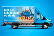 Albert Heijn bezorgwagen met promotietekst "Met één klik de zaak op de rit" en afbeeldingen van vers fruit, brood en boodschappenkratten.
