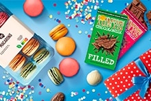 Boeket bloemen, cadeaus met blauwe strik en een blauwe boodschappenkrat gevuld met diverse producten, waaronder verzorgingsmiddelen, chocolade en drank, allemaal gepresenteerd als geschenk bij Albert Heijn.