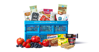 Blauwe Albert Heijn krat gevuld met verschillende snacks, granola, ontbijtkoek, fruitrepen, appels, aardbeien en blauwe bessen.
