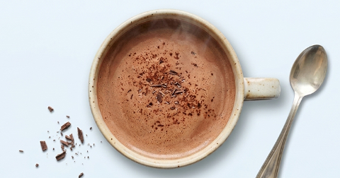 Kop warme chocolademelk met chocoladeschaafsel en een lepel ernaast