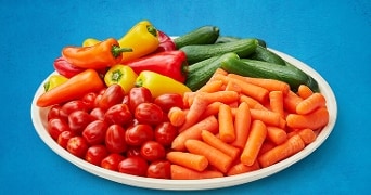 Grote schaal met een kleurrijke mix van groente, waaronder paprika's, kerstomaten, komkommers en wortelen.