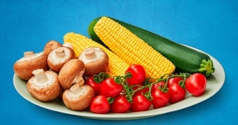 Een bord met champignons, maïs, cherrytomaten en een courgette.