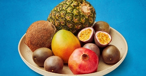 Tropische vruchten op een bord, waaronder een ananas, kokosnoot, mango, passievrucht en granaatappel.