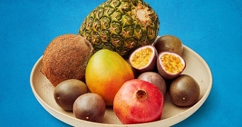 Tropische vruchten op een bord, waaronder een ananas, kokosnoot, mango, passievrucht en granaatappel.