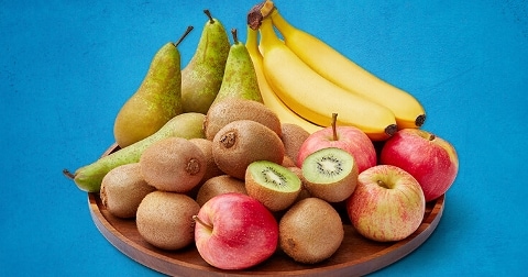 Assortiment van fruit met bananen, kiwi's, peren en rode appels op een houten schaal.