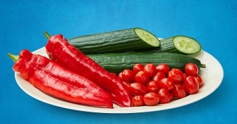 Een bord met rode paprika's, komkommers en cherrytomaten.