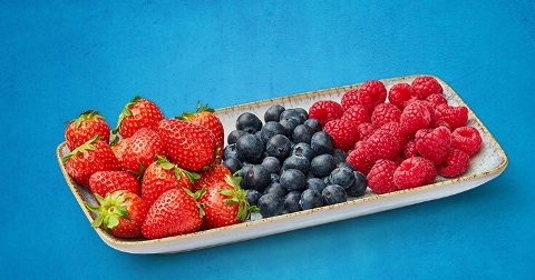 Schaal met aardbeien, blauwe bessen en frambozen op een blauwe achtergrond.