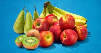 Fruit selectie met peren, bananen, appels, nectarines en kiwi's op een blauwe achtergrond.