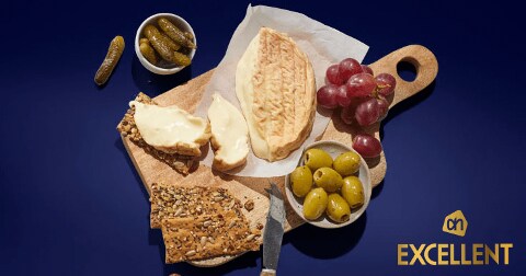 Luxe borrelplank met AH Excellent kaas, crackers, groene olijven, druiven en augurken op een houten serveerplank.