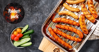 Gegrilde worstjes in een metalen braadslee met cherrytomaatjes en komkommer, met tekst "Pakket park".