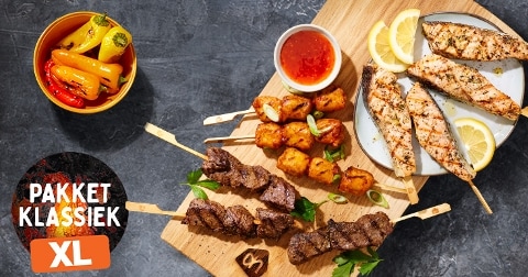 Pakket Klassiek XL met verschillende vlees- en kipspiesen, een schaaltje gegrilde paprika's, saus en citroen op een serveerplank.