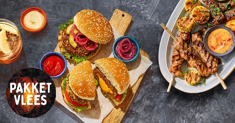 Twee hamburgers met sesambroodjes, geserveerd op een houten plank met sausjes en rode uien, naast een schaal met vlees- en groentespiesjes en dipsaus. Tekst op de afbeelding: "Pakket Vlees".
