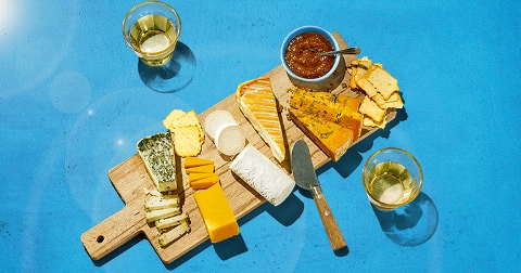 Borrelplank met diverse kazen, crackers, dips en twee glazen witte wijn op een blauwe achtergrond.