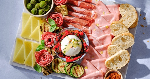 Charcuterieplank met een assortiment van vleeswaren, kazen, olijven, burrata, rozemarijn en sneetjes brood.