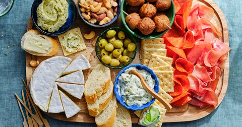 Assortiment van kaas, vleeswaren, olijven, noten, en dips op een houten serveerplank.