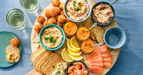 Borrelplank met gerookte zalm, toastjes, diverse dips, citroenschijfjes en borrelhapjes op een houten dienblad.