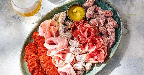 Schaal met vleeswaren en dip, geserveerd met een glas bier.