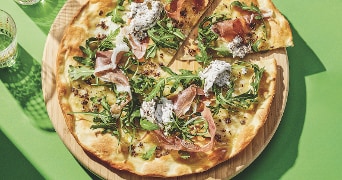 Pizza met prosciutto, rucola en ricotta op een groene achtergrond.